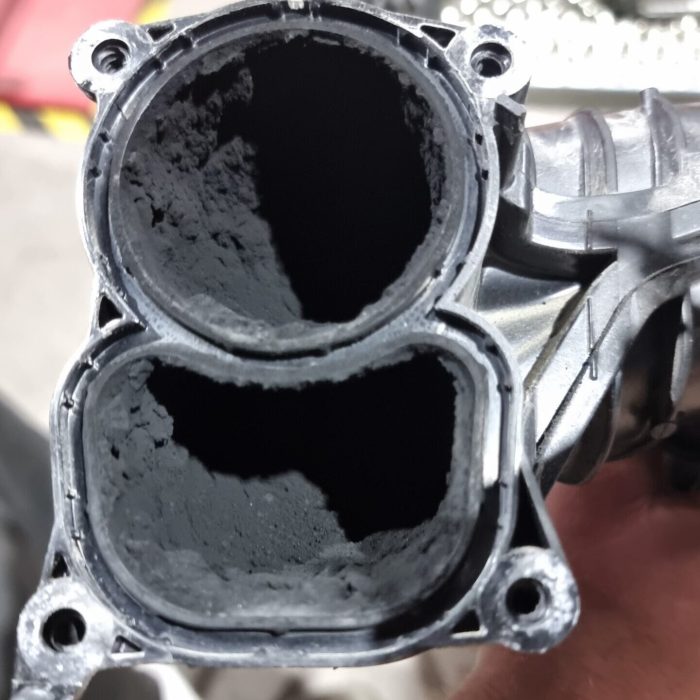 En insugsdel av en motor fylld med sot innan rengöring